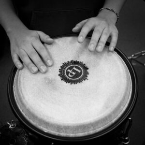 A black and white close-up shot of hands drumming on a bongo drum, emphasizing rhythm and music.