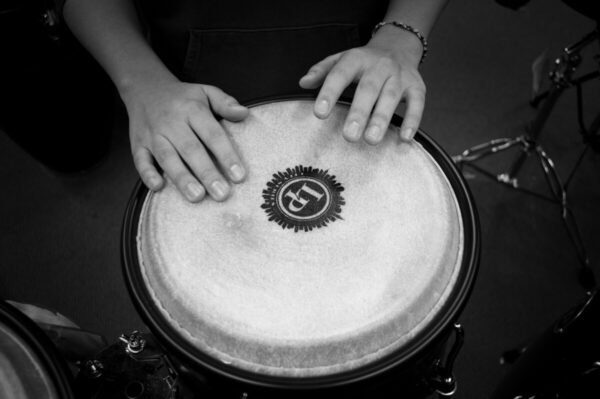 A black and white close-up shot of hands drumming on a bongo drum, emphasizing rhythm and music.