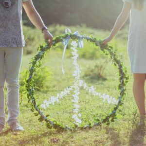 A couple holding a floral peace symbol outdoors in a sunny meadow.